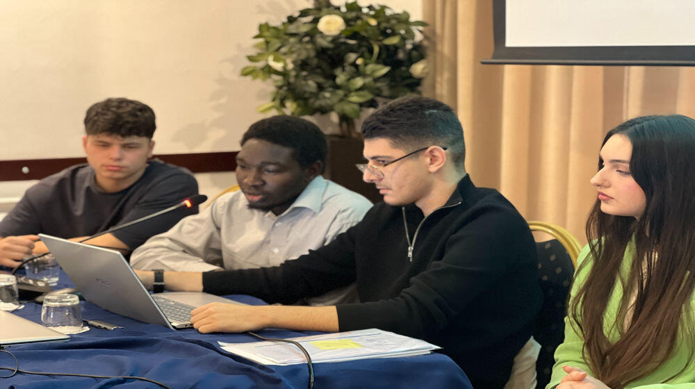 New generation of peacebuilders in Albania during a training. There are 3 boys and a girl sitting around a table, reading in the PC in front of them.