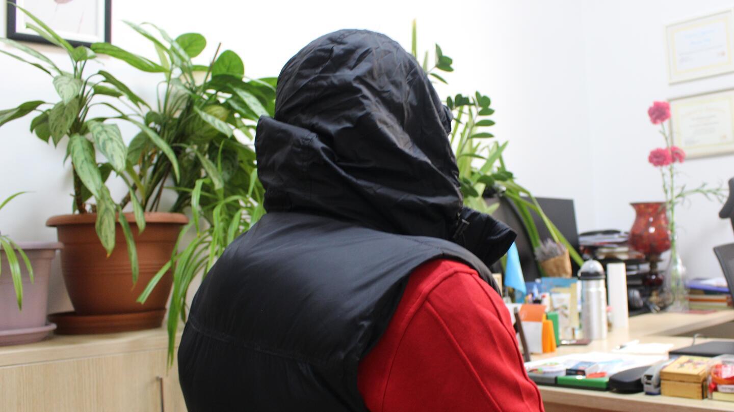 "Andi," a young man living with HIV, dressed in sportswear and wearing a hood, photographed from behind to protect his anonymity.